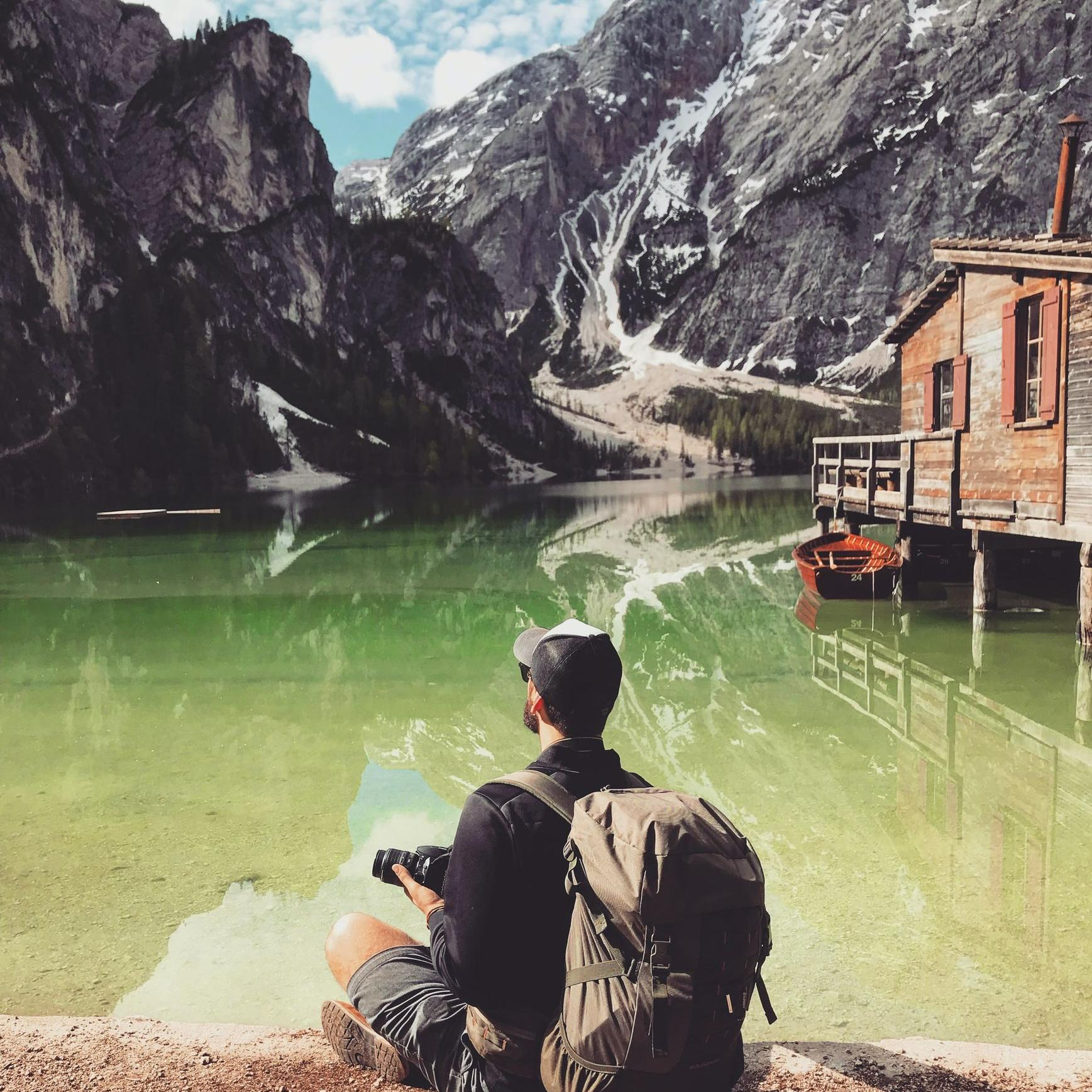 man in brown jacket sitting on brown rock near body of water during daytime